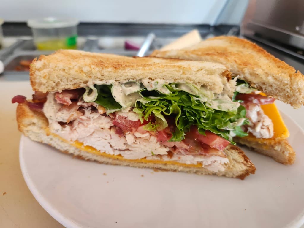 Stacked club sandwich with greens, tomato, and sliced chicken