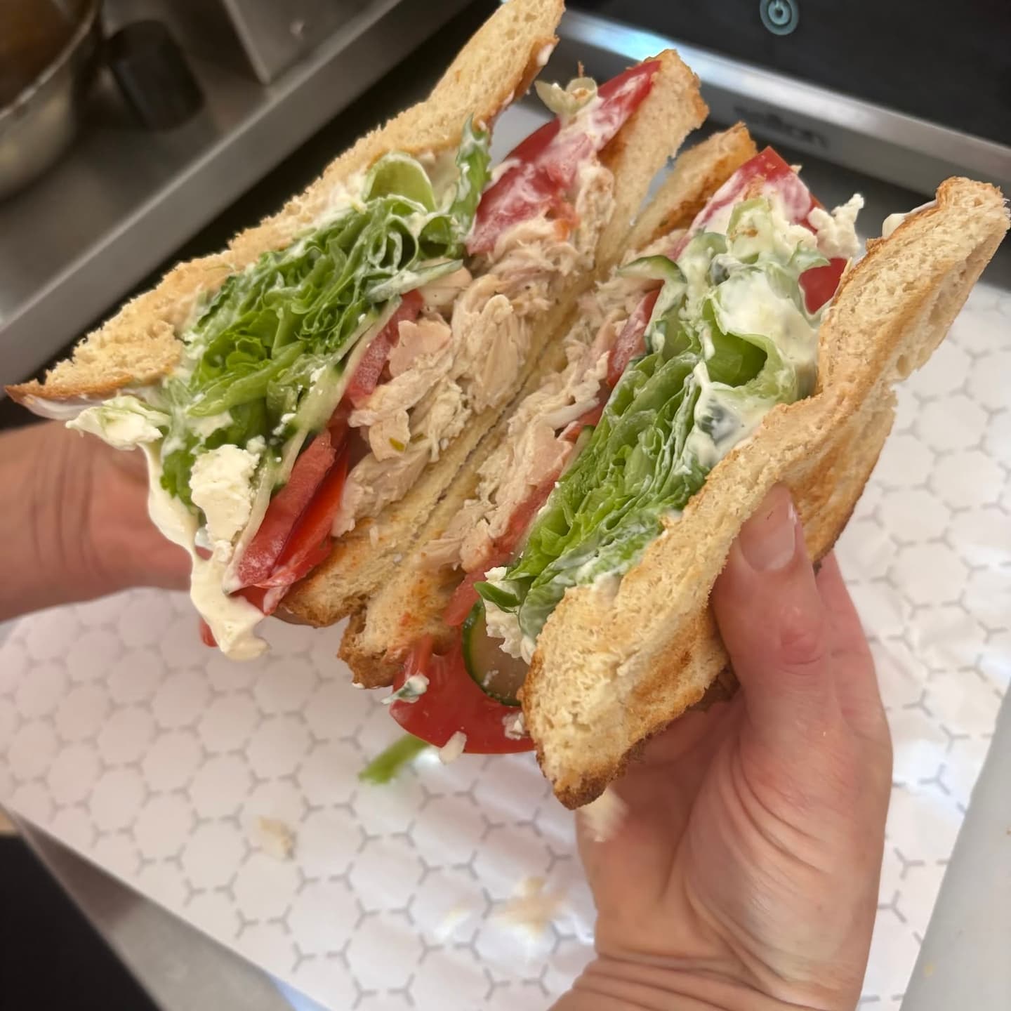 Stacked club sandwich with greens, tomato, and sliced chicken on toasted bread